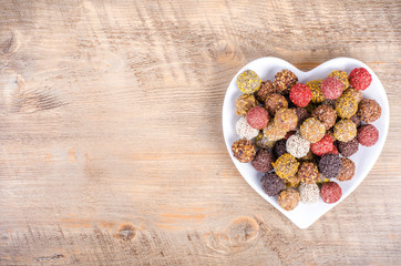 Handmade chocolate candies on plate forming heart, wooden background. Free space for your text.