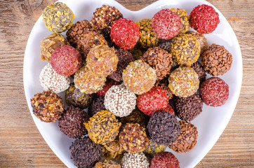 Handmade chocolate candies on plate forming heart, wooden background. Free space for your text.