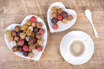 Handmade chocolate candies on plate forming heart, wooden background. Free space for your text.