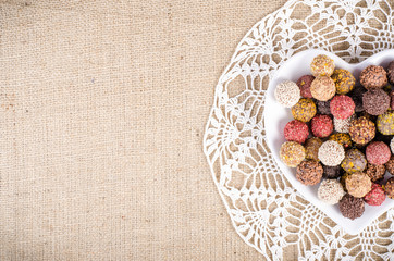 Handmade chocolate candies on plate forming heart, knitted cloth, sackcloth, canvas. Free space for your text.