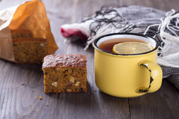 Homemade carrot and banana cake with nuts and spices, a cup of tea with lemon on a wooden surface