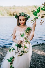 The young bride in a wreath stands near water