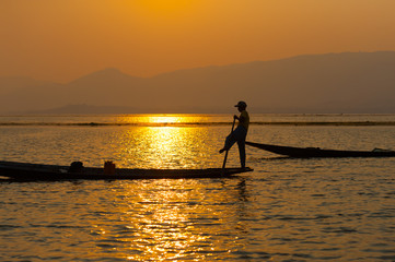 INLE LAKE VILLAGE MYANMAR : Silhouette People rows the wooden boat by his leg in Inle Lake