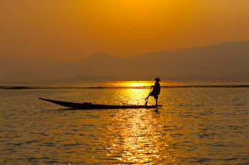 Naklejka na ściany i meble INLE LAKE VILLAGE MYANMAR : Silhouette People rows the wooden boat by his leg in Inle Lake