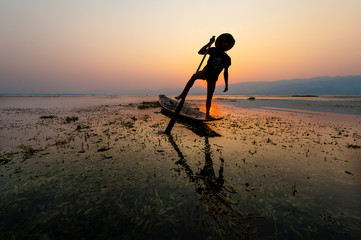 INLE LAKE VILLAGE MYANMAR : Silhouette People rows the wooden boat by his leg in Inle Lake