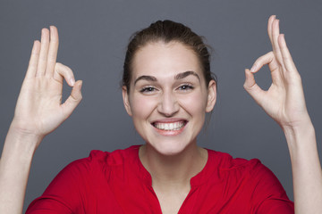 radiant approval concept - thrilled 20s girl smiling with double ok for satisfaction and success,studio shot on gray background