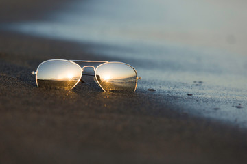 Sunglasses reflect the light of the setting sun at sandy beach