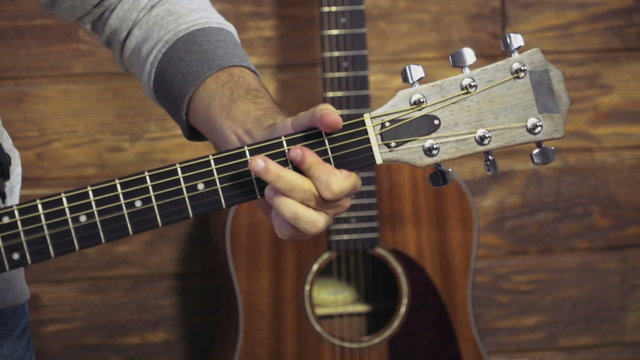close up mans hand taking chords on acoustic guitar slow motion