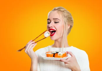 Photo sur Plexiglas Bar à sushi Young woman holding sushi with a chopsticks, isolated on yellow