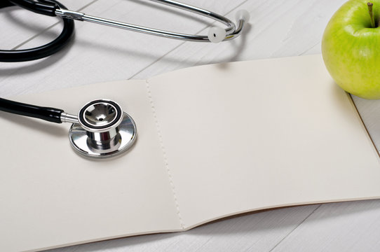 Open notebook with blank pages with stethoscope and apple