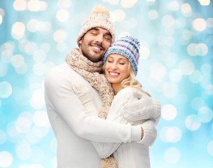 happy couple in winter clothes hugging over lights