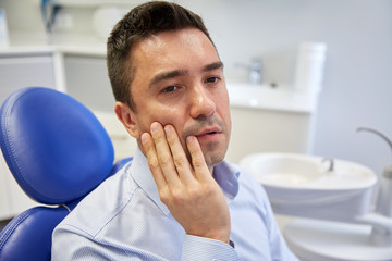 man having toothache and sitting on dental chair