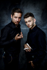 Elegant young handsome men.  Man with straight razor and man holding hairdressers scisors