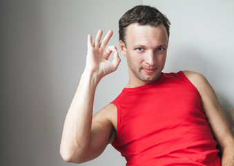 Young smiling man in red shirt shows okay gesture