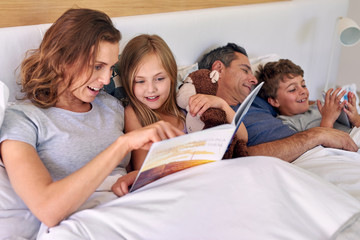 Happy family lying in bed with book and tablet device