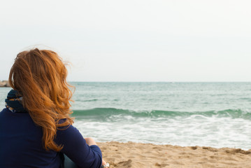 Fototapeta na wymiar Redhead girl on a Barcelona sand beach looking at the sea, view from behind