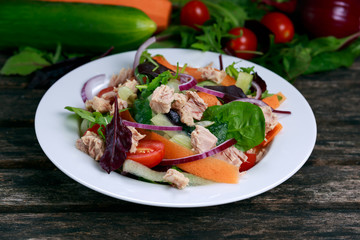 Tuna salad with Spinach, rocket, red ruby chard, tomatoes, cucumbers, carrot, red onion on old wooden table