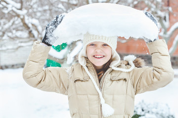 Cheerful young girl holding piece of snow over her head