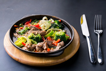 beef stew with vegetables in a frying pan over dark background