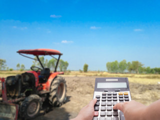 Investment cost concept by calculator and the blur farm and tractor in background