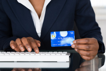 Person's Hand Holding Credit Card While Typing On Keyboard