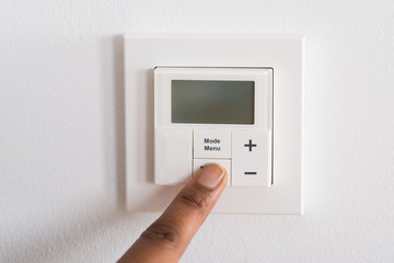 Person's Finger Adjusting Room Temperature On Digital Thermostat