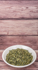 Dried Japanese green tea leaves in white bowl over wooden background