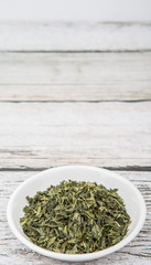 Fototapeta na wymiar Dried Japanese green tea leaves in white bowl over wooden background