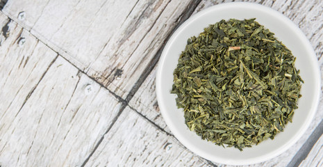 Dried Japanese green tea leaves in white bowl over wooden background
