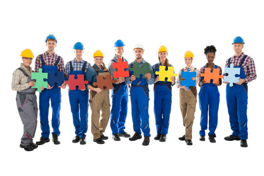 Confident Construction Workers Holding Jigsaw Pieces In Row