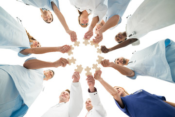 Medical Team Joining Jigsaw Pieces In Huddle - obrazy, fototapety, plakaty