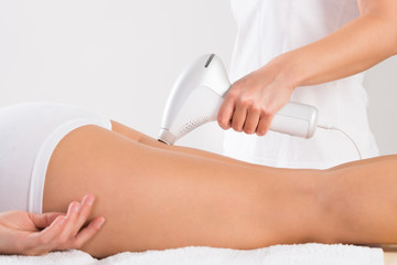 Obraz na płótnie Canvas Beautician Using Laser Machine On Young Customer's Leg