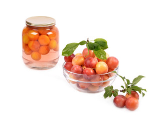 Jar of cherry plum compote and fresh plums in a glass container on a white background