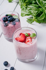 Smoothie with strawberries and blueberries in a glass on a white wooden background with basil 