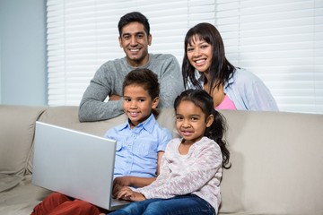 Smiling family using laptop on sofa