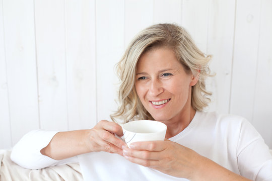 beautiful adult woman with blond hair, smiling, happy drinking coffee, tea.He is sitting on the sofa with a cup in hand. 