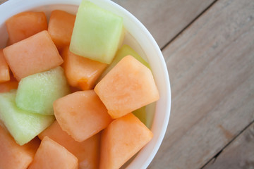 closeup melon slice in white dish with wood table background