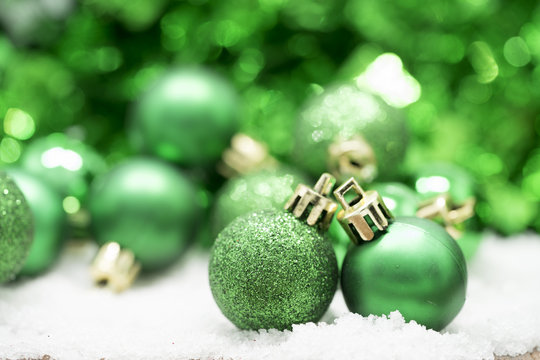 Green Christmas balls on snow against green bokeh background