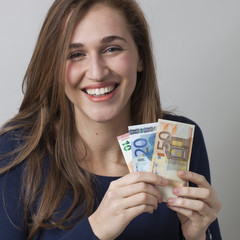 value for money concept - portrait of laughing 20s woman holding Euro bills for valuable earnings or economic wellbeing,studio shot