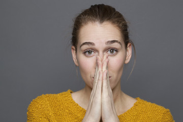 negative feelings concept - playful beautiful 20s girl covering her mouth and nose with both hands for fun mistake or bad odor,studio shot on gray background