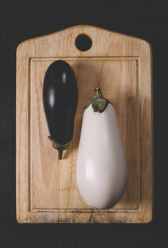 White and purple eggplant on a cutting board on a black wooden background with a free space top view