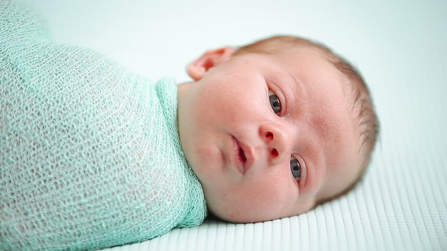 Blue-eyed newborn baby lying and looking around in wonder