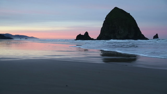 Haystack Rock, Cannon Beach Dawn. Sunrise at Haystack Rock in Cannon Beach, Oregon as the surf washes up onto the beach. United States.

