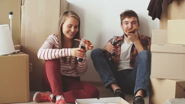 Young couple sitting on the floor in their new house and eating pizza