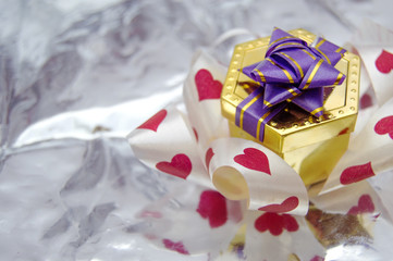 Gift box with hearts ribbon, on silver background.