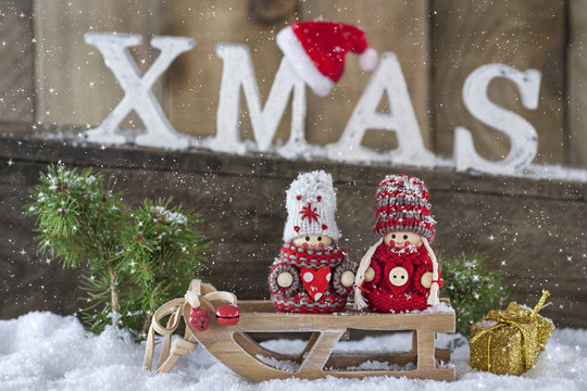 Zwei Wichtel vor weihnachtlichem Hintergrund im Schnee unter Holzbuchstaben XMAS