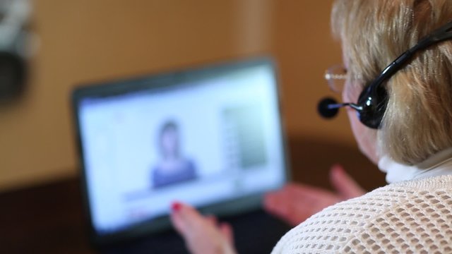 Woman with headphones with microphone talks to a customer via computer. Woman communicates via laptop

