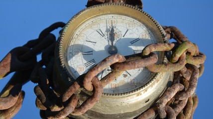 Vintage clock in chains against blue sky