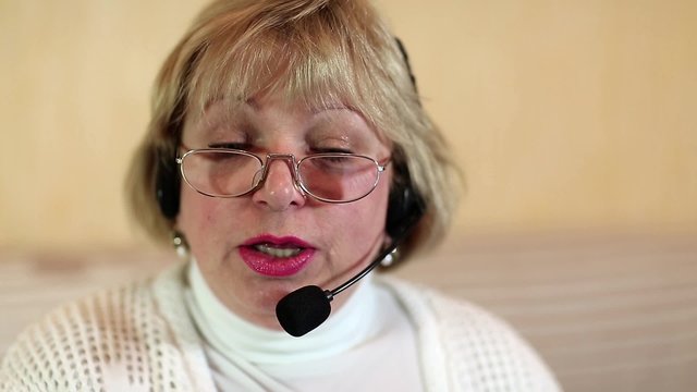Blonde woman with headphones with microphone looks at the camera and talks to a client
