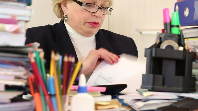 Blonde woman chief financial officer in glasses and with commercial papers sits at the table. Trouble at work. Bookkeeper with commercial papers
